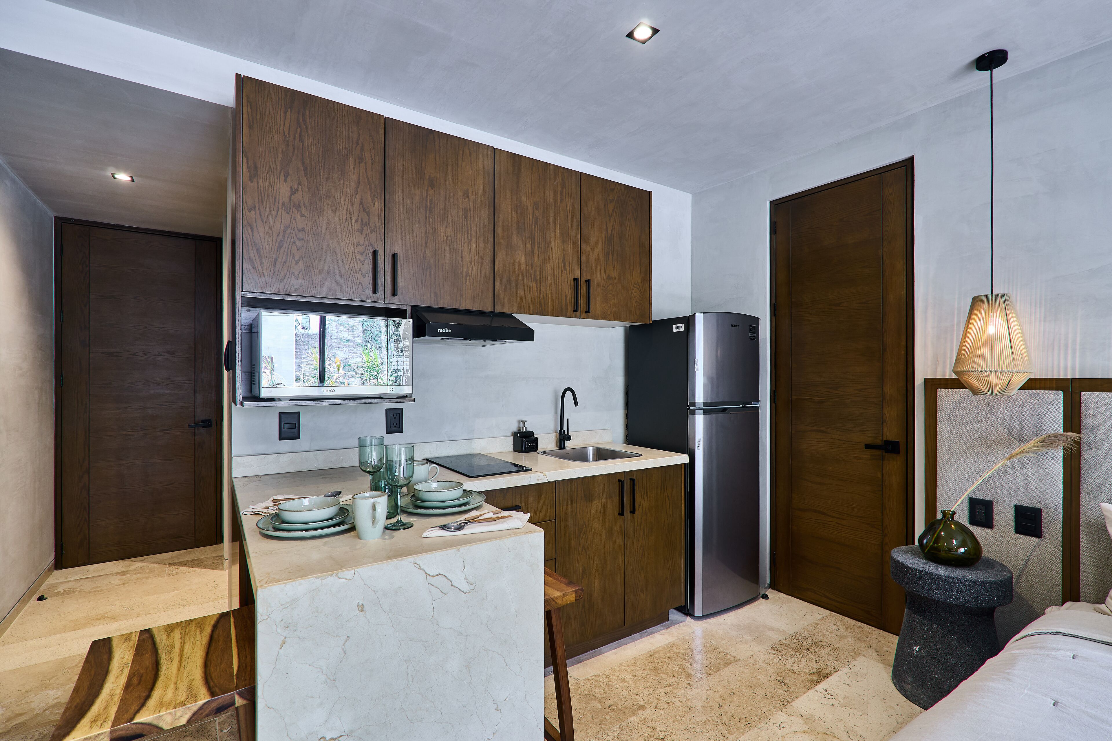A compact kitchen with wooden cabinets, a stainless steel refrigerator, and a small dining area.