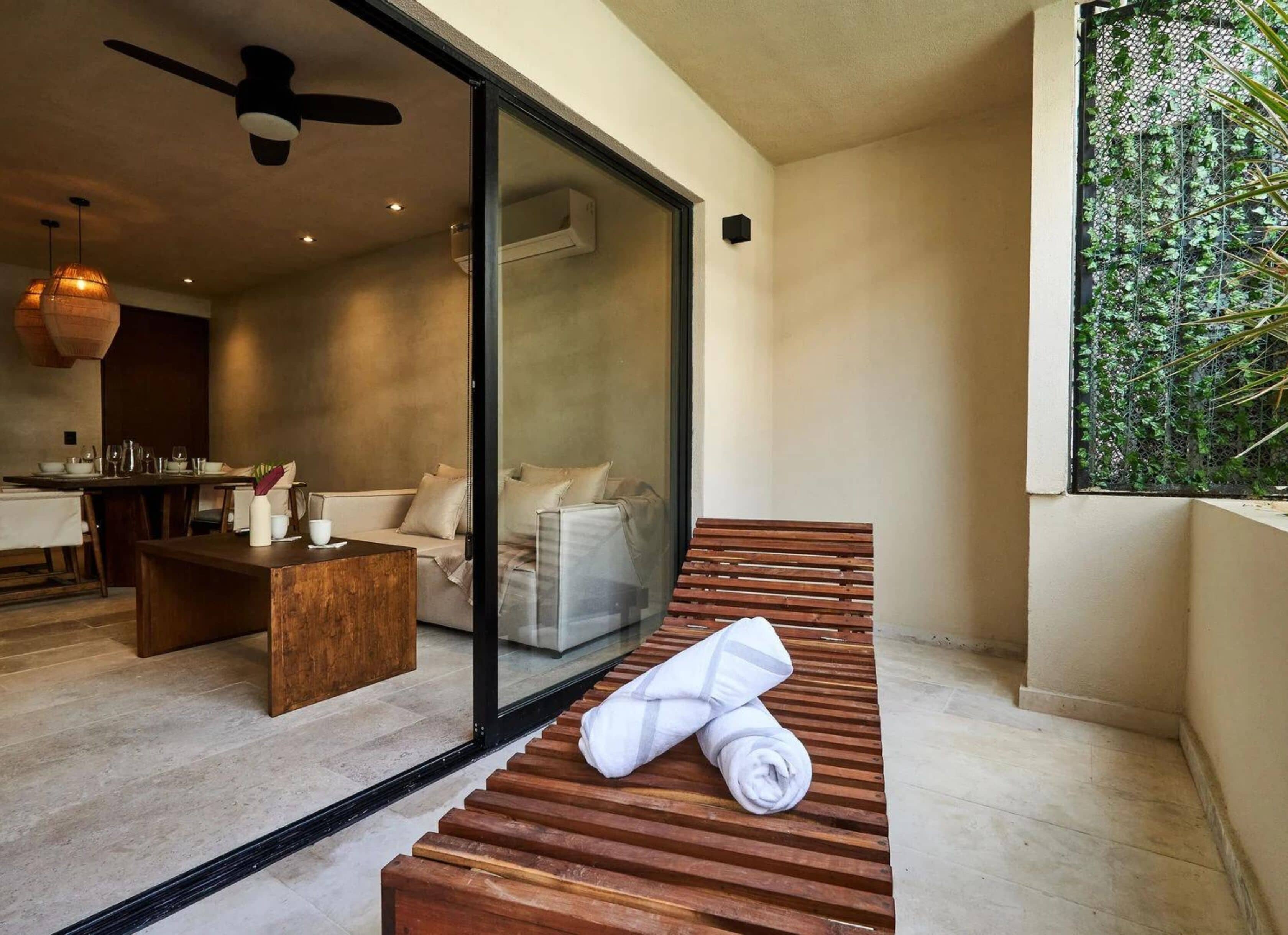 A modern interior with a wooden bench, a glass door leading to a dining area, and a green wall with foliage.