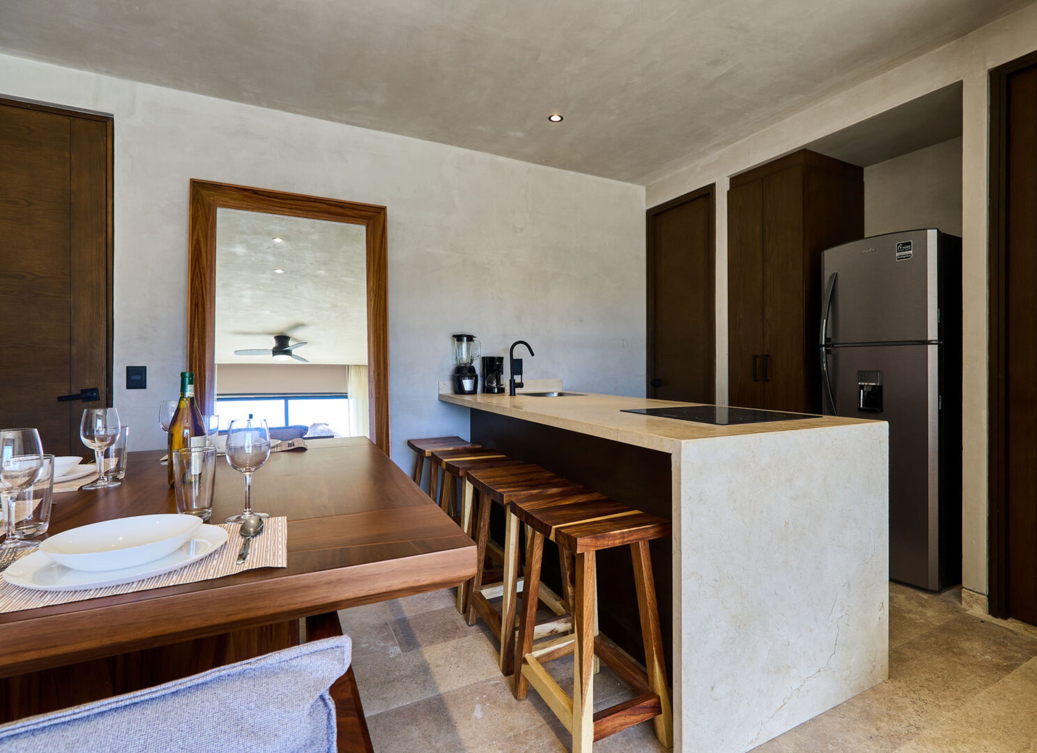 A modern kitchen with a central island, wooden stools, a built-in oven, and a refrigerator.