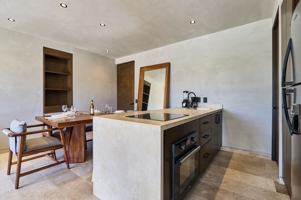 A modern kitchen with a central island, built-in oven, and a dining area with a wooden table and chairs.