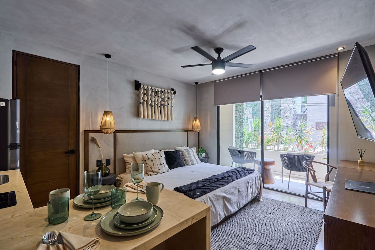 A modern bedroom with a bed, bedside table, and a view of the outdoors through large windows.