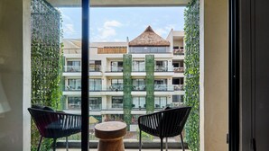 Ein Balkon mit zwei schwarzen Stühlen und einem Holztisch mit Blick auf ein Gebäude mit einem Strohdach und Balkonen.