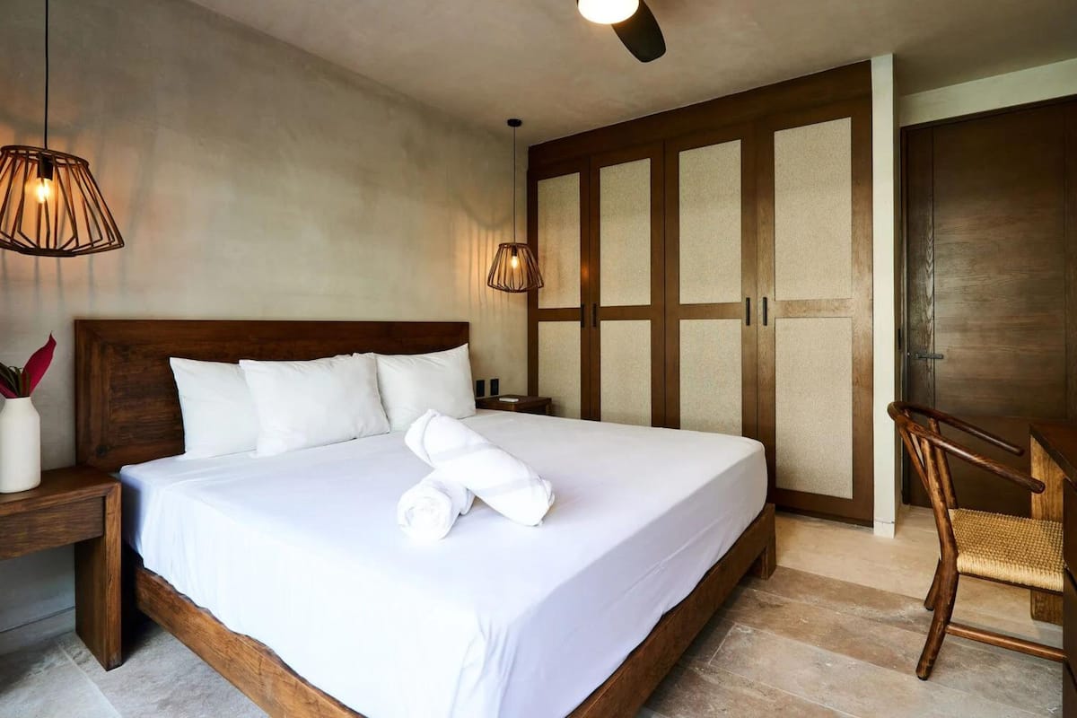A hotel room with a large bed, wooden headboard, two bedside lamps, a ceiling fan, and a wardrobe with frosted glass panels.