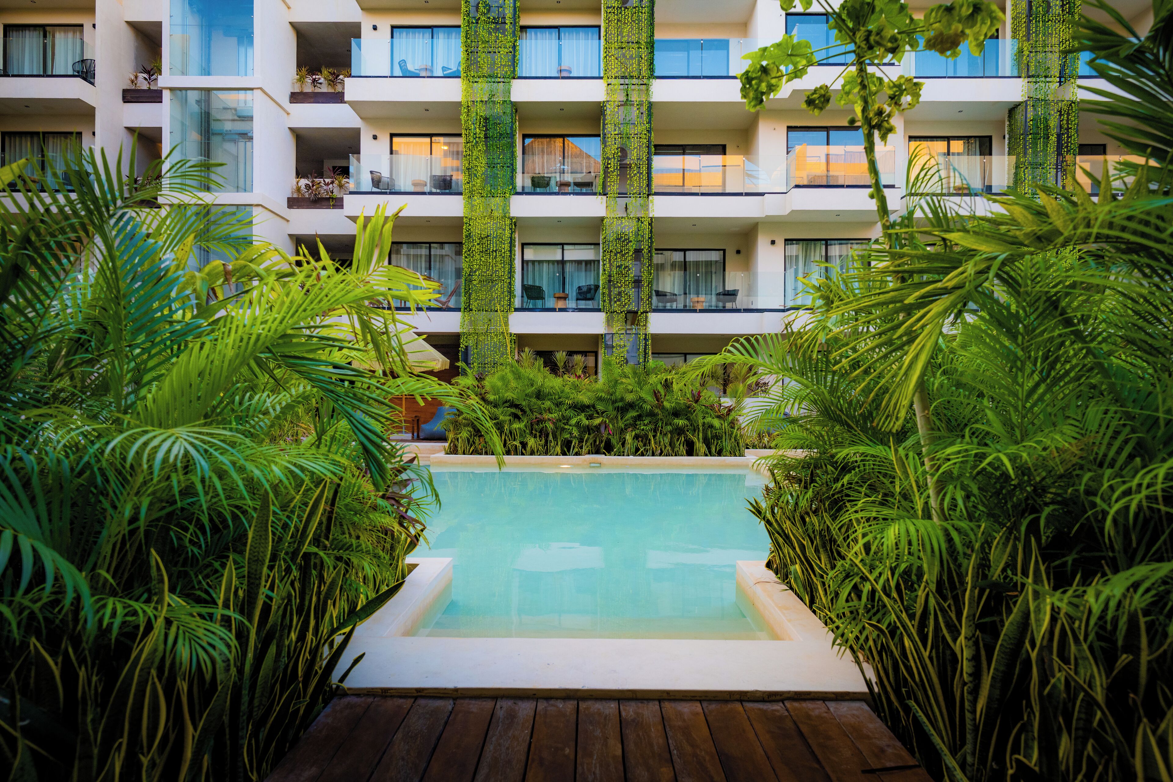 A pool surrounded by lush greenery, with a multi-story building in the background.