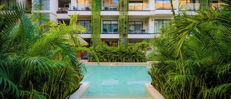 A pool surrounded by lush greenery, with a multi-story building in the background.