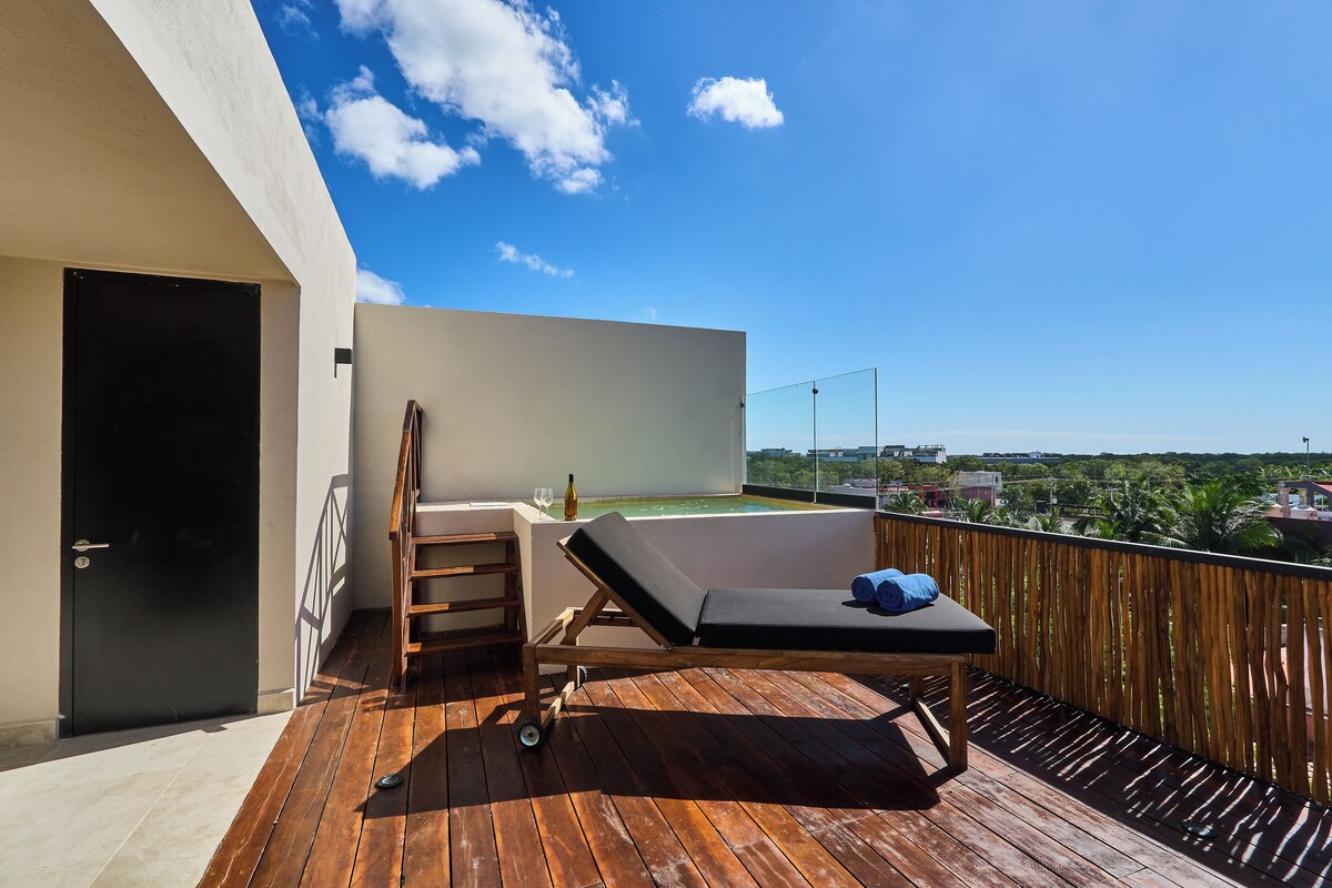 A wooden deck with a lounge chair and a small table, a door, and a view of a cityscape.