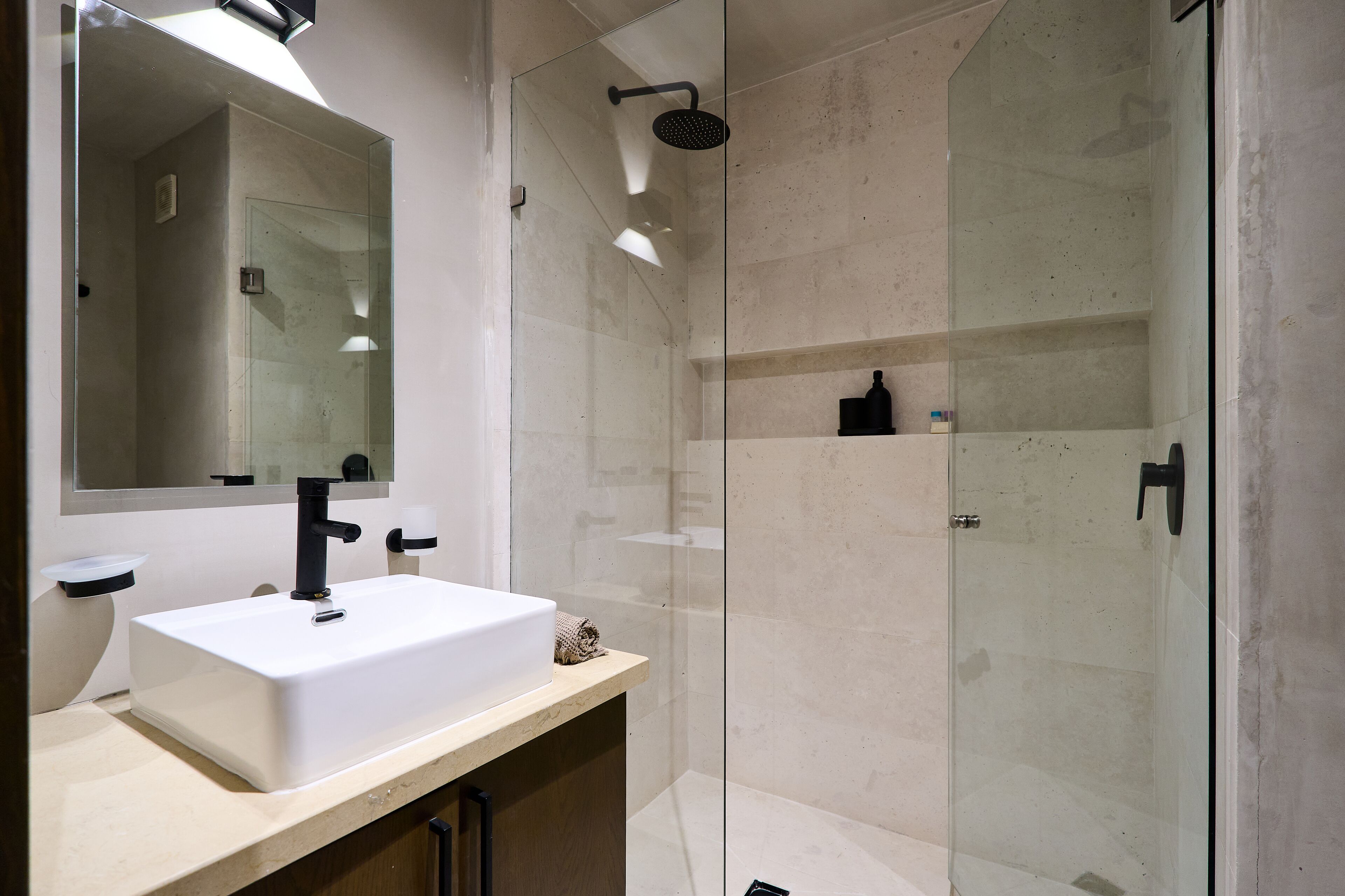 A modern bathroom with a white sink, a large mirror, and a glass-enclosed shower area.