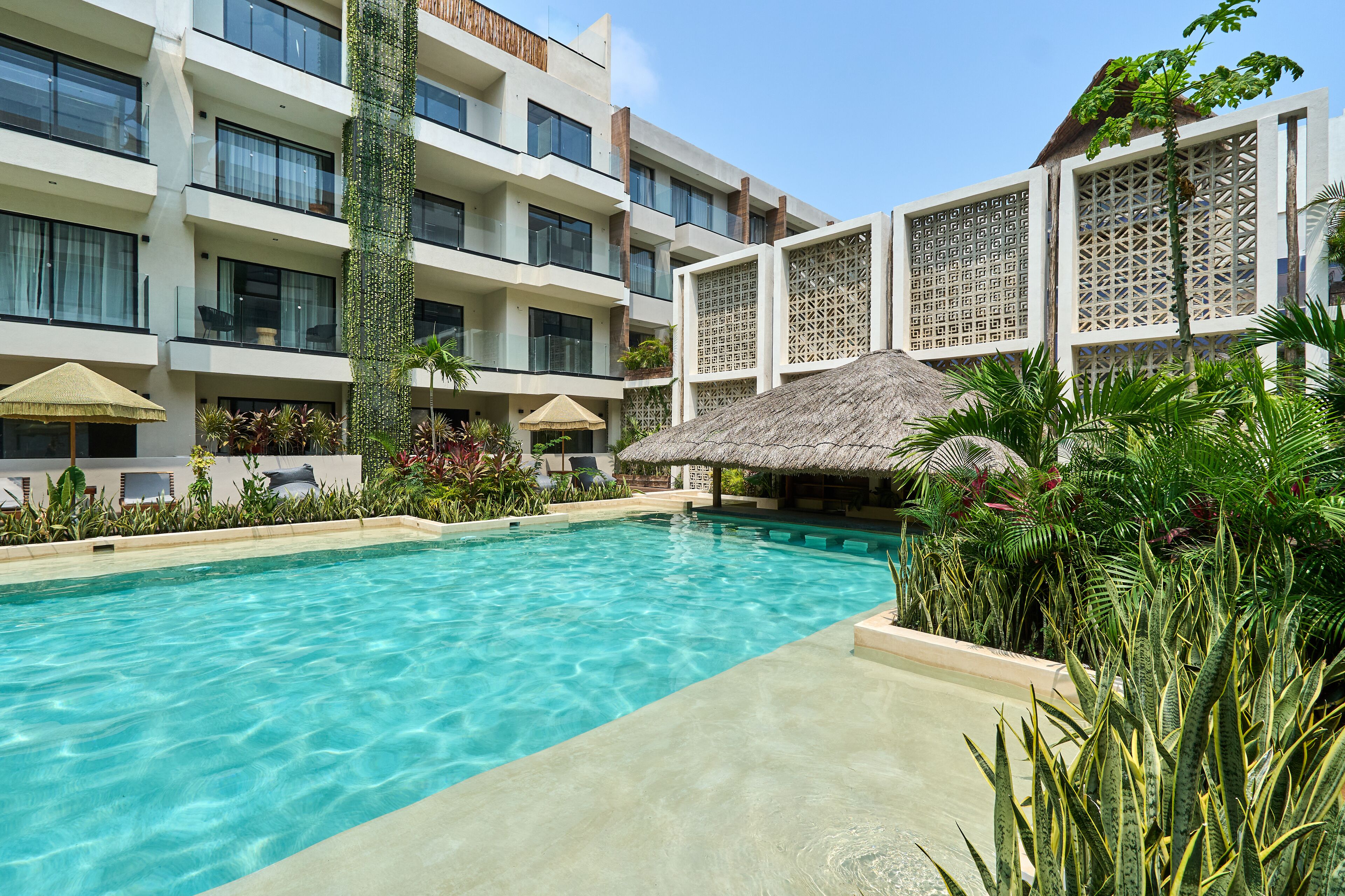 A swimming pool surrounded by lush greenery and a modern building with multiple balconies.