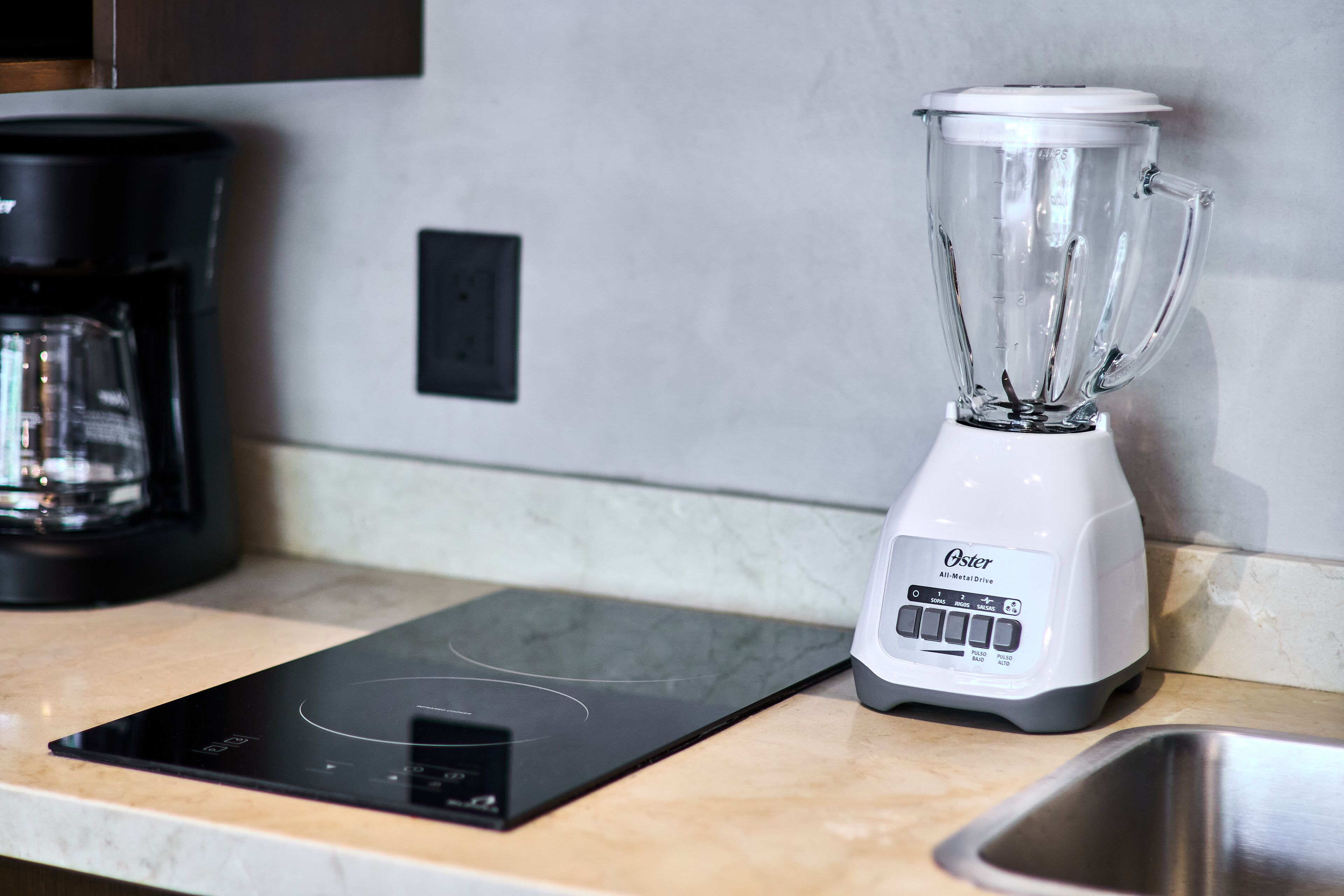 Une cuisine dotée d’une plaque de cuisson à induction noire, d’un mixeur Oster tout en métal et d’un évier en acier inoxydable.