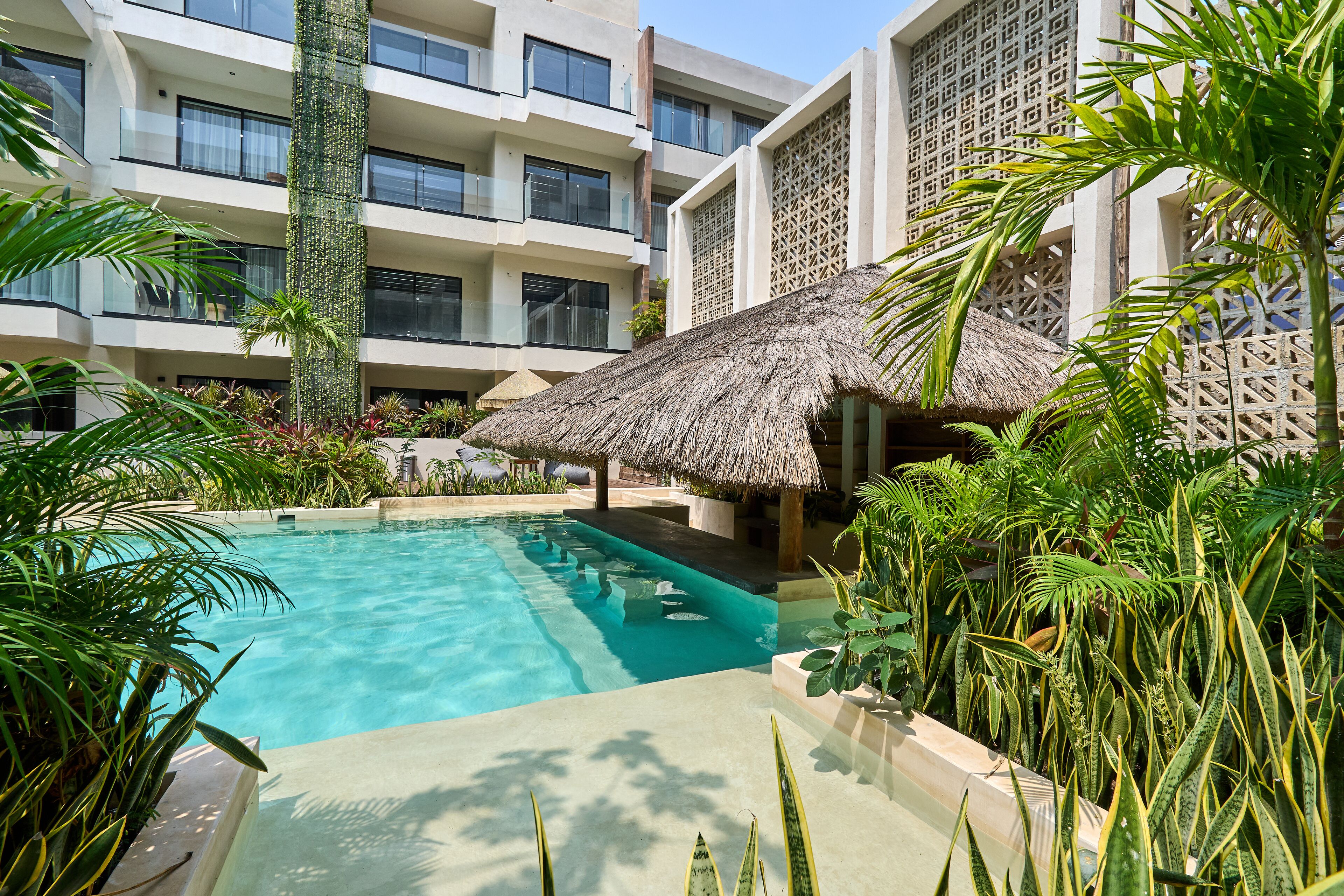 A swimming pool surrounded by lush greenery and a thatched-roof structure.