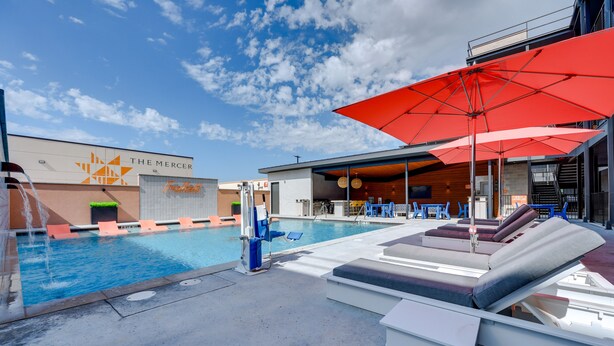A pool area with lounge chairs, a red umbrella, and a building with 'THE MERCER' signage. - Pet-Friendly New Braunfels Condo w/ Shared Pool! (New Braunfels)