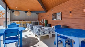 A modern outdoor seating area with blue tables and chairs, a wooden ceiling, and a kitchen in the background. - Pet-Friendly New Braunfels Condo w/ Shared Pool! (New Braunfels)