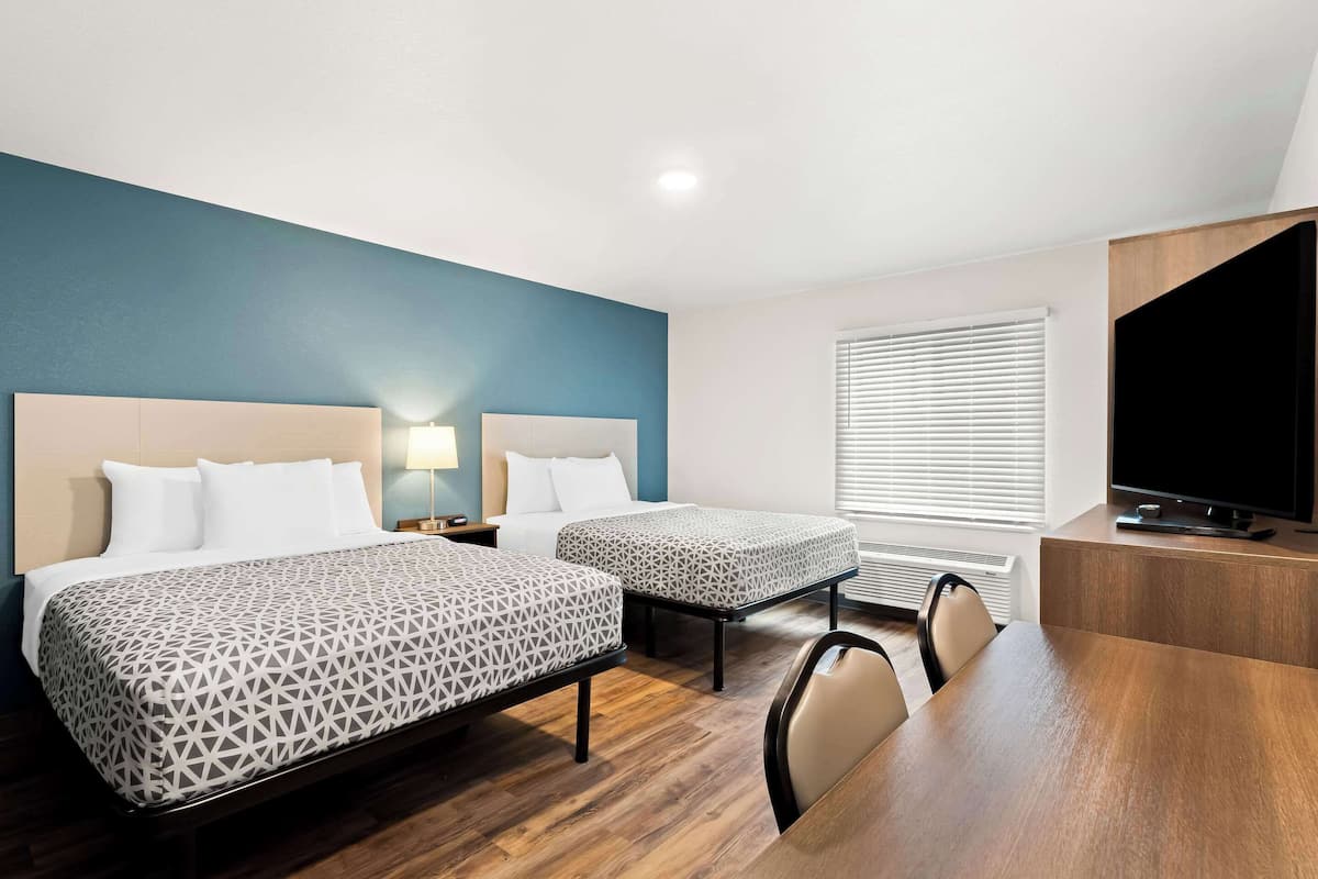 A hotel room with two beds, a desk, a chair, a TV, and a window with blinds.