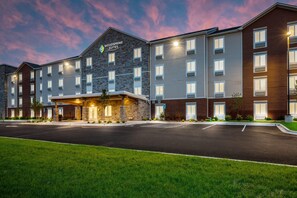 A multi-story hotel with a stone facade, a covered entrance, and a parking lot. - Woodspring Suites Denver Commerce City (Commerce City)