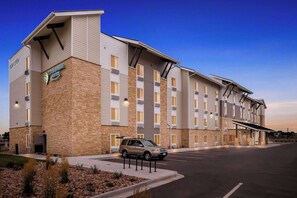 A multi-story hotel with a brick facade, a parking lot, and a clear sky. - Woodspring Suites Denver Commerce City (Commerce City)