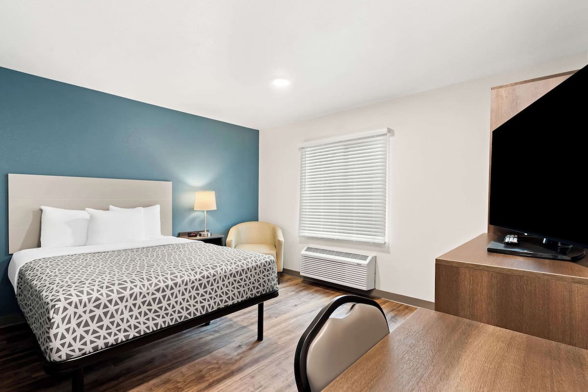 A hotel room with a bed, a desk, a chair, a television, a lamp, and a window with blinds.