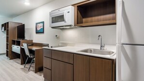 Cocina compacta con armarios de madera, microondas, lavabo y refrigerador.