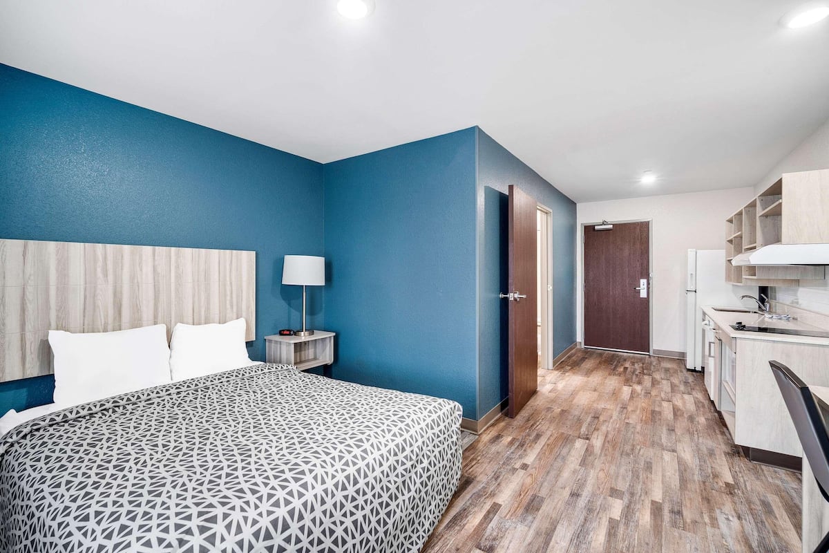Ein Hotelzimmer mit Bett, Nachttisch, Lampe und einer Küchenzeile.