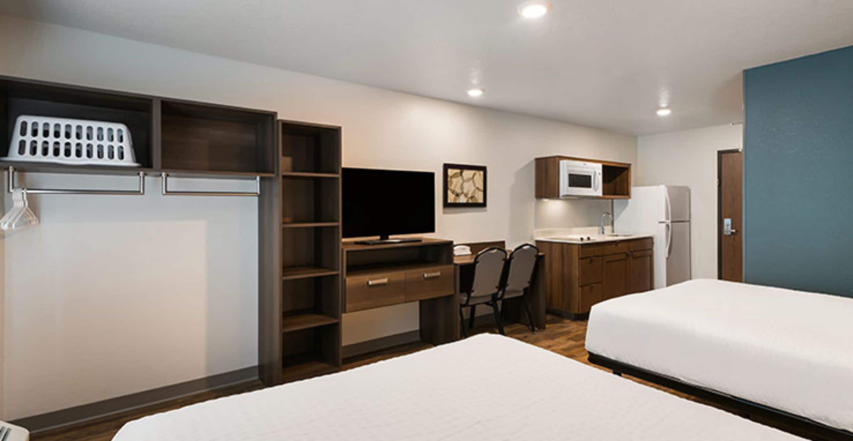 A hotel room with a bed, a desk with a computer, a TV, a microwave, and a small kitchenette.