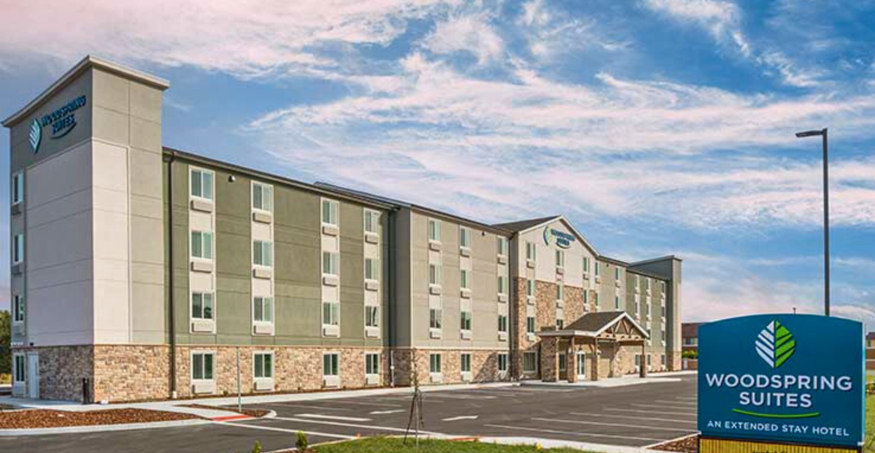 A hotel with a modern design, featuring a central entrance with a covered area, multiple floors, and a parking lot in front.