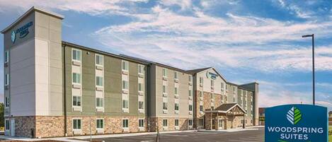A hotel with a modern design, featuring a central entrance with a covered area, multiple floors, and a parking lot in front.