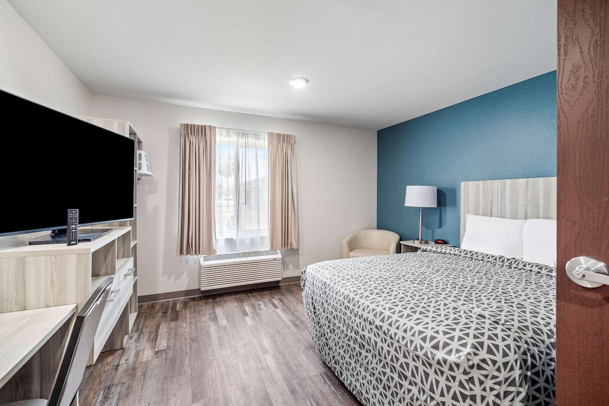 Ein Hotelzimmer mit Bett, Schreibtisch, Stuhl, Fernseher und einem fensterbepflanzten Fenster.