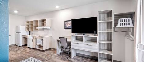 A modern, compact living space with a kitchenette, a flat-screen TV, a dining area, and a built-in wardrobe.