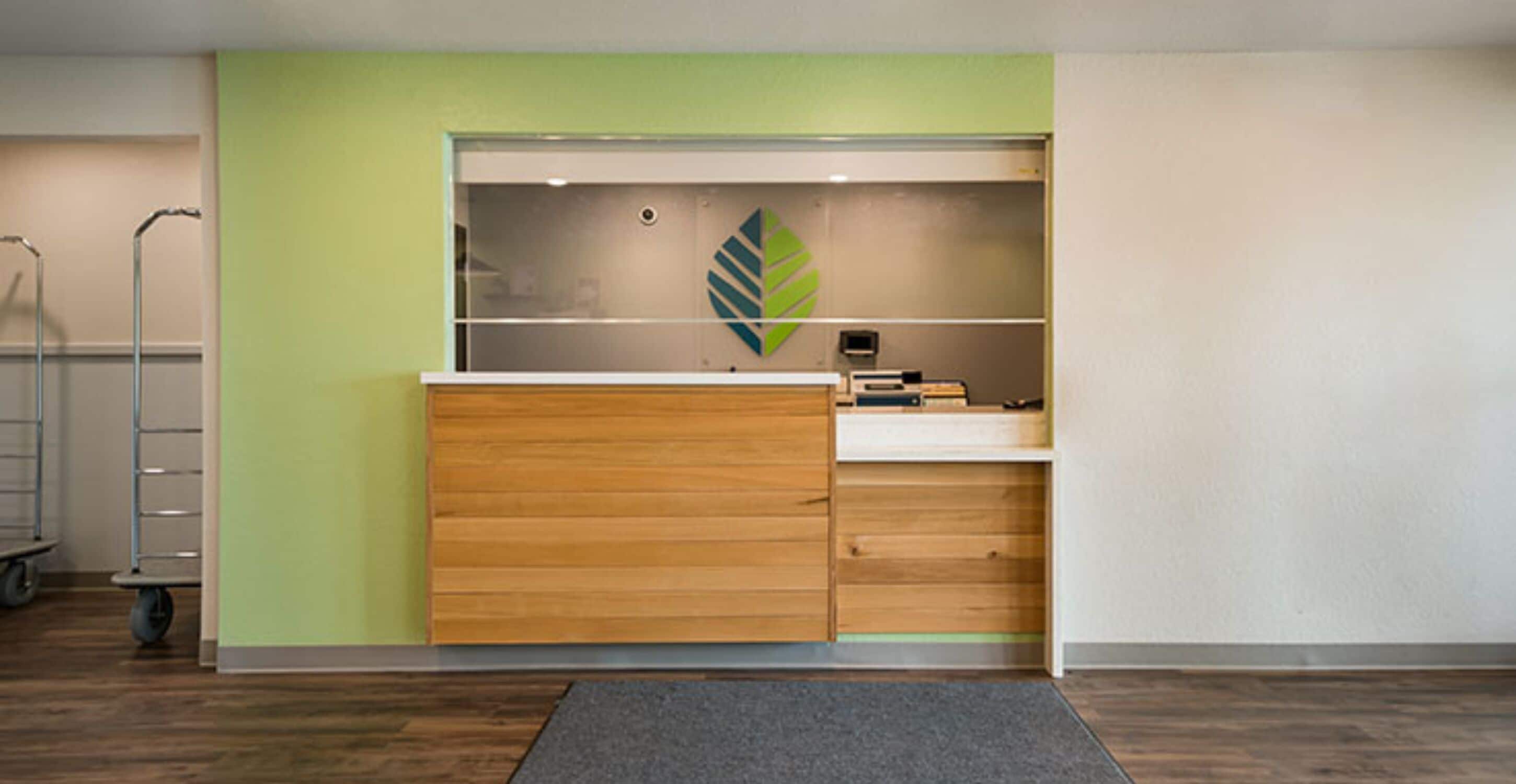 Un mostrador de recepción con una pared verde, un logo con forma de hoja y una alfombra gris.