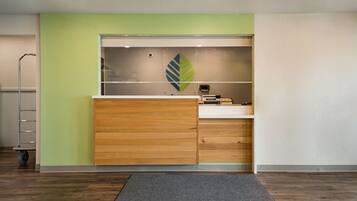 Un mostrador de recepción con una pared verde, un logo con forma de hoja y una alfombra gris.