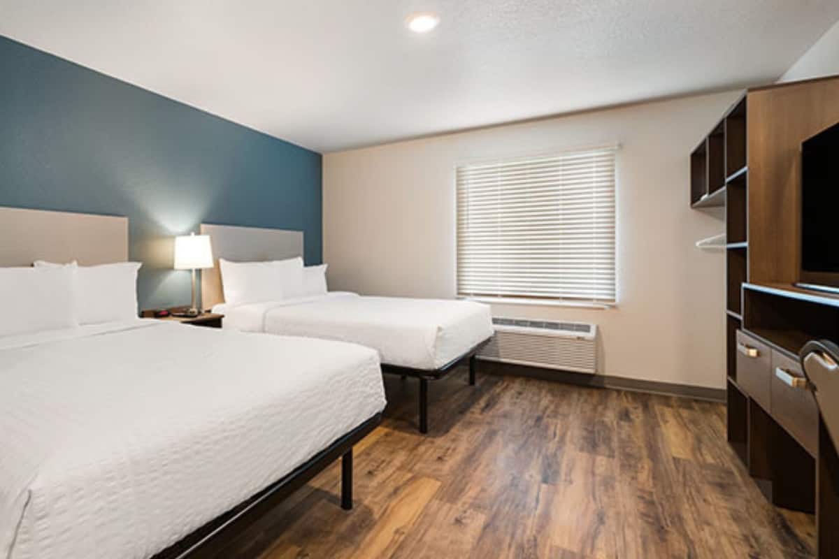 Une chambre d’hôtel avec deux lits, un bureau, une armoire et une fenêtre avec des stores.