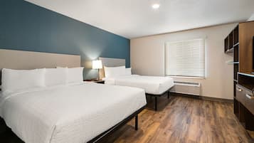 Une chambre d’hôtel avec deux lits, un bureau, une armoire et une fenêtre avec des stores.