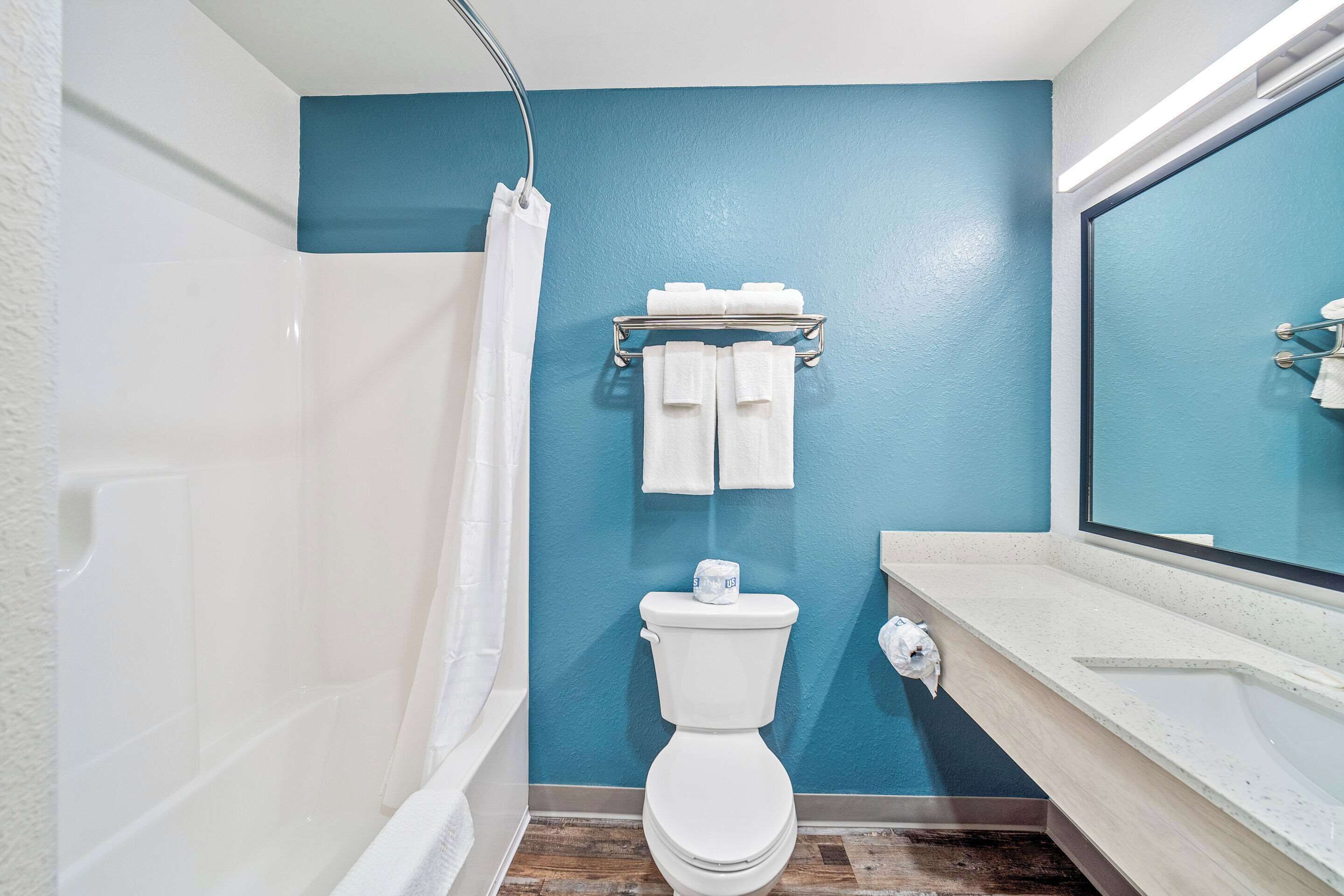 Une salle de bain avec un mur bleu, des toilettes blanches et un rideau de douche.