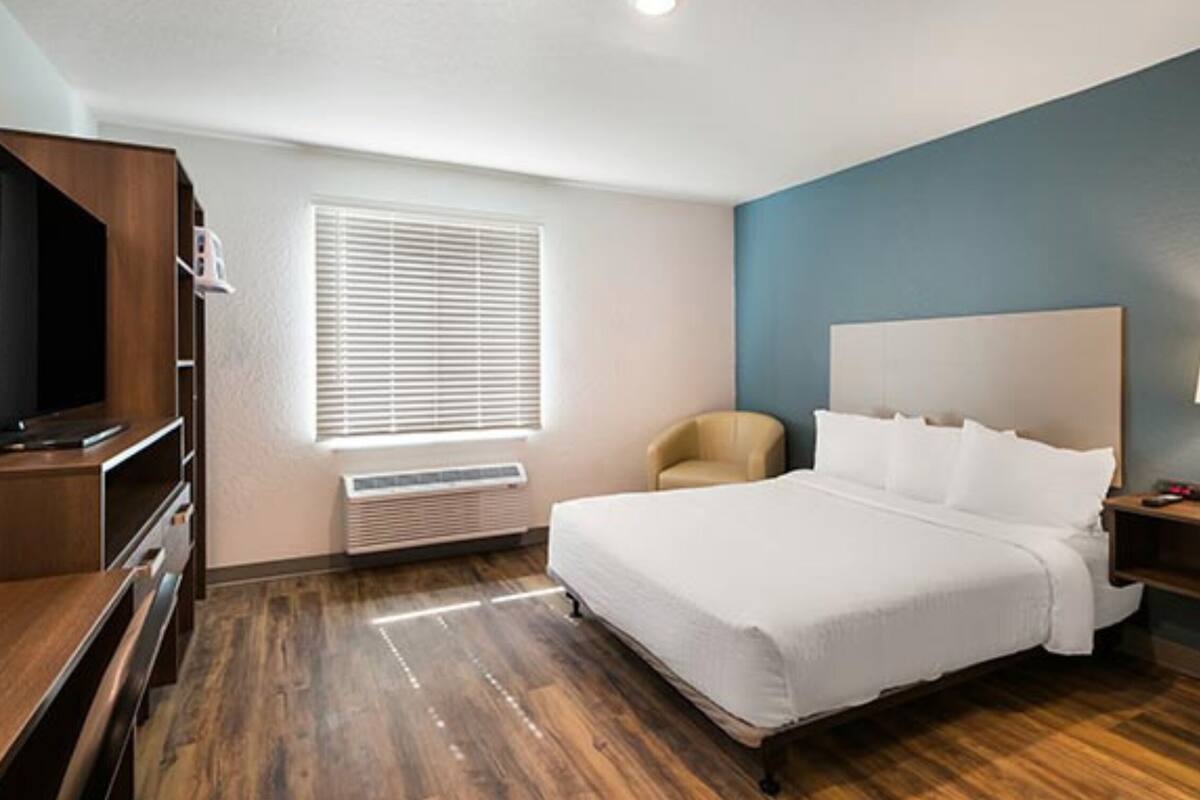 Une chambre d’hôtel équipée d’un lit, d’un bureau, d’une chaise, d’une télévision, d’une lampe et d’une fenêtre avec des stores.