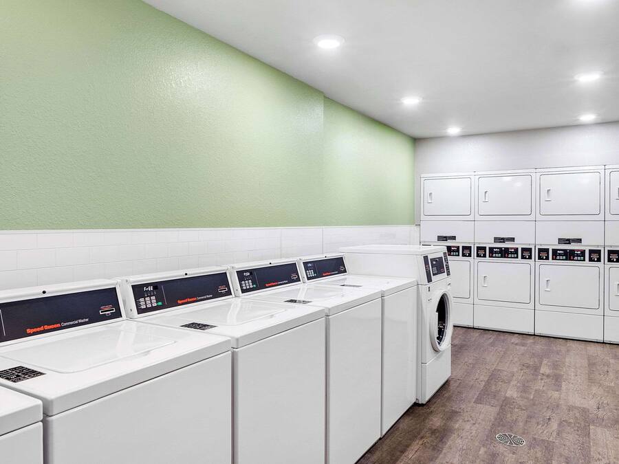 Un moderno cuarto de lavandería con varias lavadoras y secadoras, gabinetes blancos y una pared de acento verde.