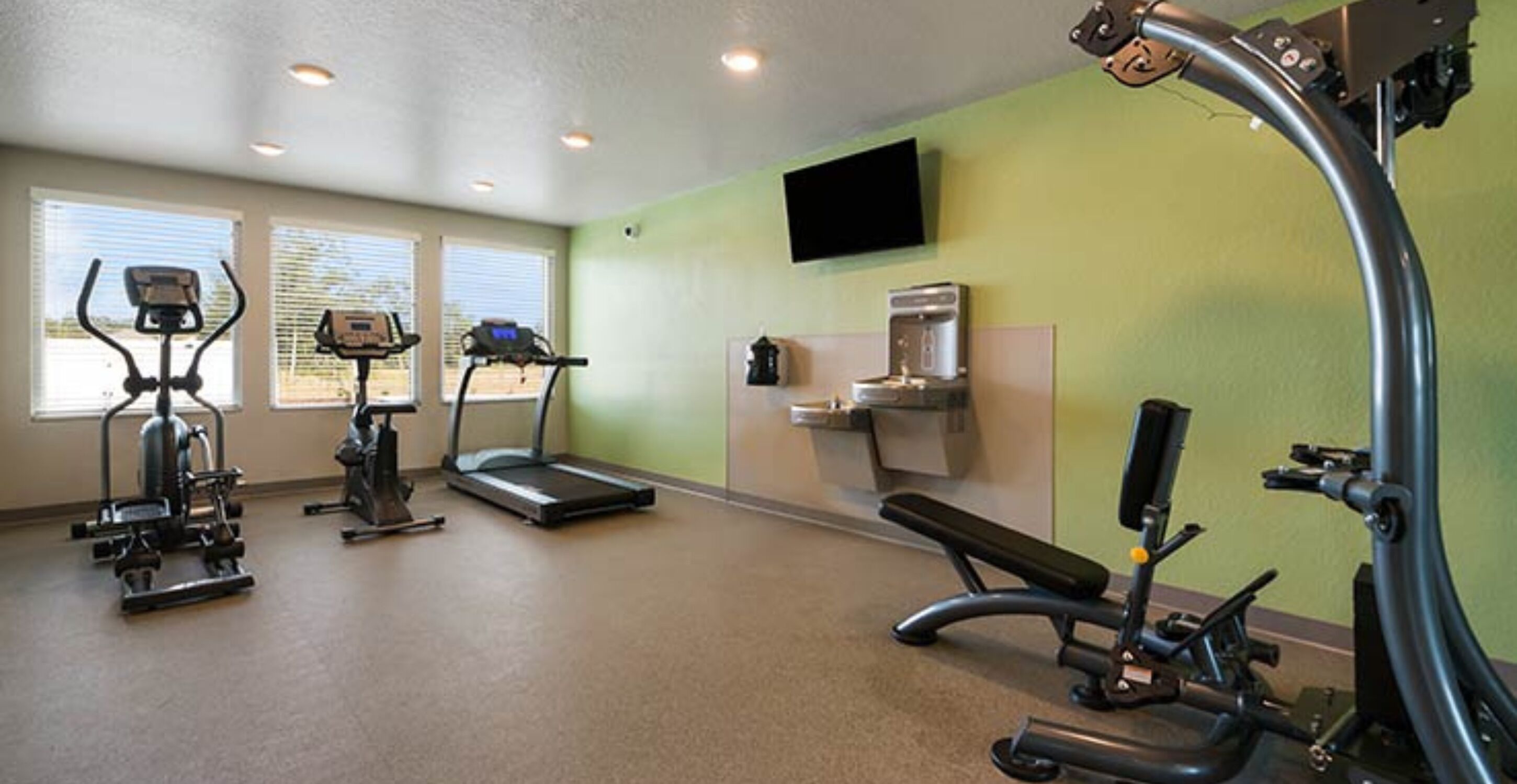 Une salle de sport équipée de tapis de course, de vélos elliptiques, d’un banc de musculation et d’un distributeur d’eau.