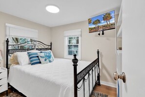 Ein Schlafzimmer mit einem Bett, einem Nachttisch, einem Fenster und einem Bild an der Wand.