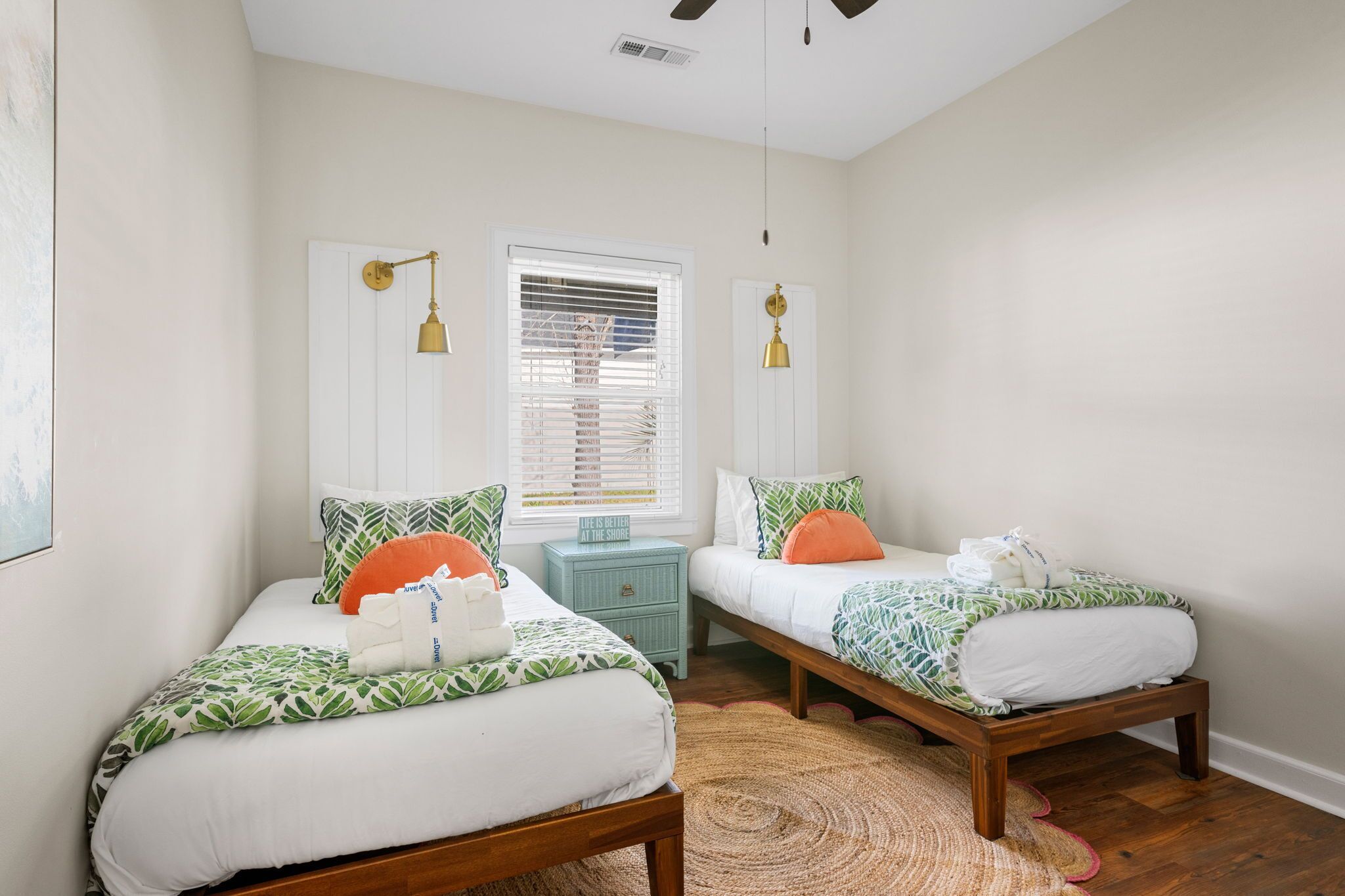 A bedroom with two single beds, a small nightstand, a window with blinds, and a ceiling fan.