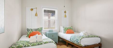 A bedroom with two single beds, a small nightstand, a window with blinds, and a ceiling fan.