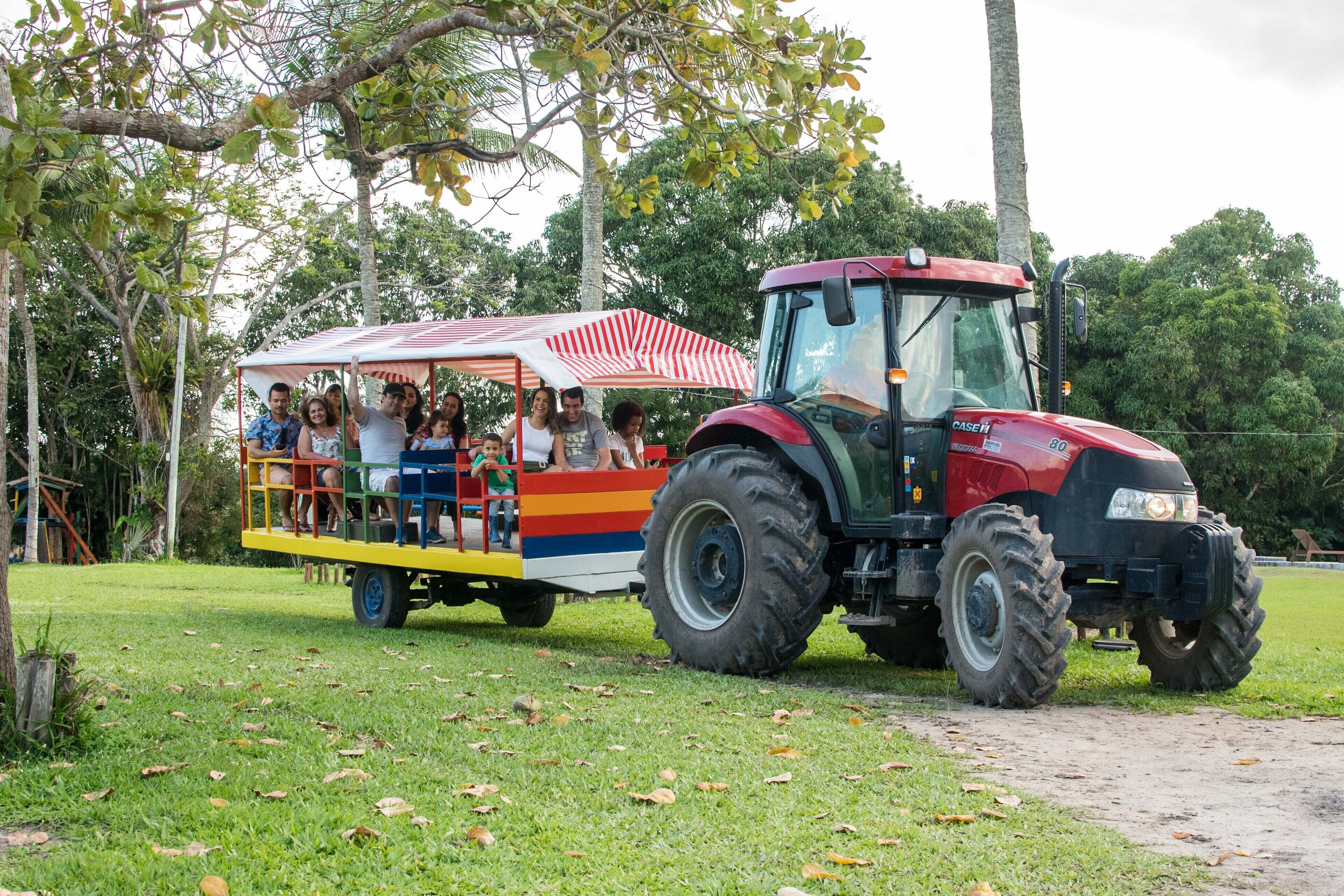 A red tractor pulling a colorful trailer with people on it.