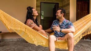 A couple sitting in a hammock on a patterned floor, with a wooden door and a window in the background. - Hotel Fazenda Mirage (Conceição de Jacuípe)