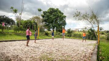 A volleyball game on a sandy court surrounded by greenery and trees.
