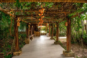 Une allée couverte, agrémentée de bancs et de décorations suspendues, et bordée d’une végétation luxuriante.