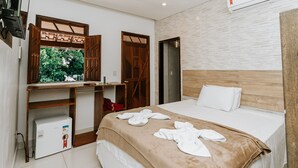 A hotel room with a bed, a wooden desk, a small refrigerator, and a window with a view of greenery. - Hotel Fazenda Mirage (Conceição de Jacuípe)