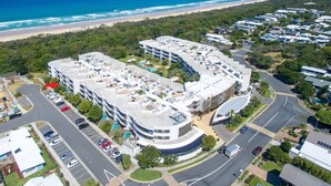Vista aérea de un hotel costero con varias construcciones, zonas de estacionamiento y una playa al fondo.