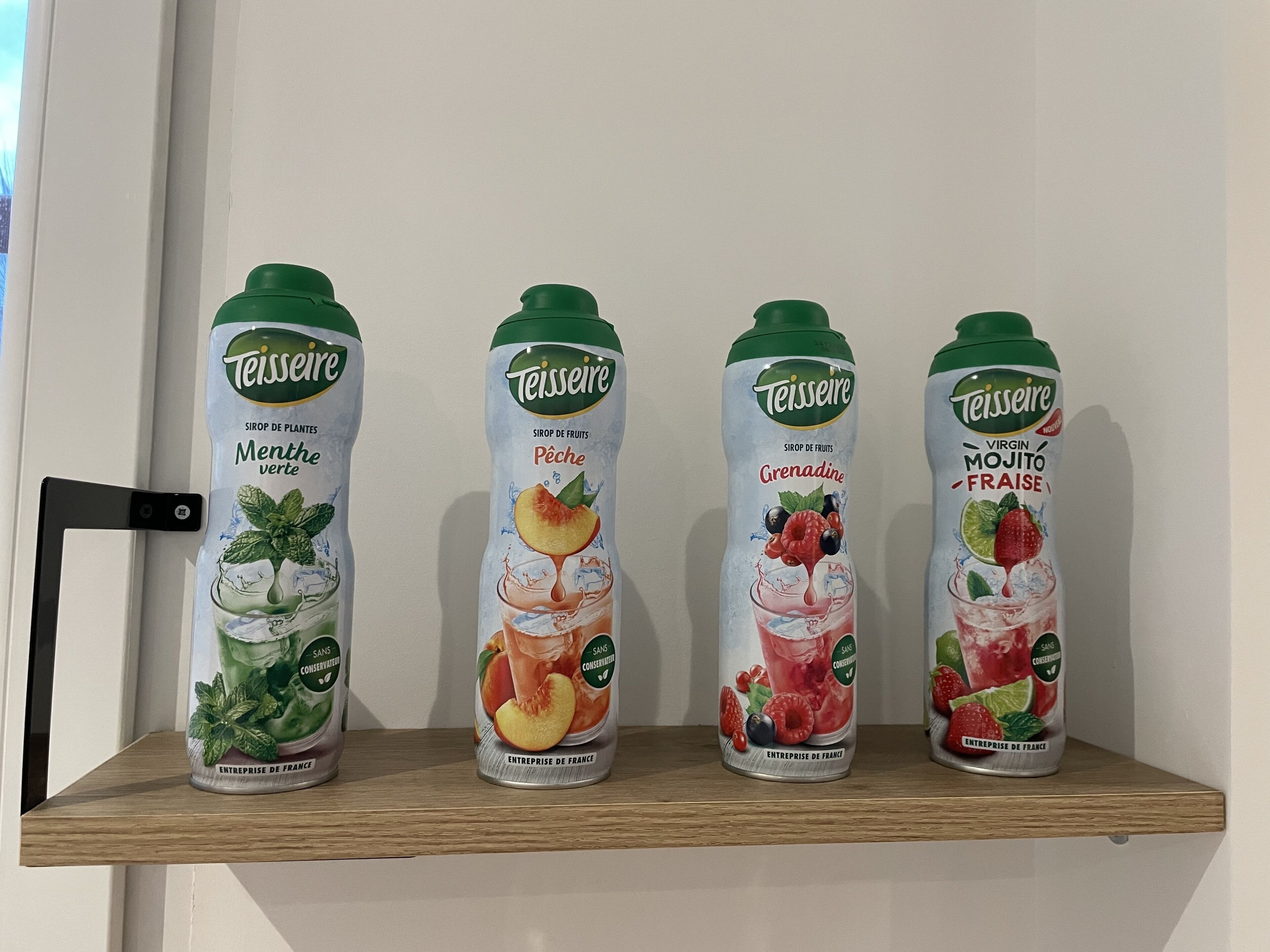 Four bottles of Teisseire fruit juice on a wooden shelf.