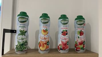 Four bottles of Teisseire fruit juice on a wooden shelf.
