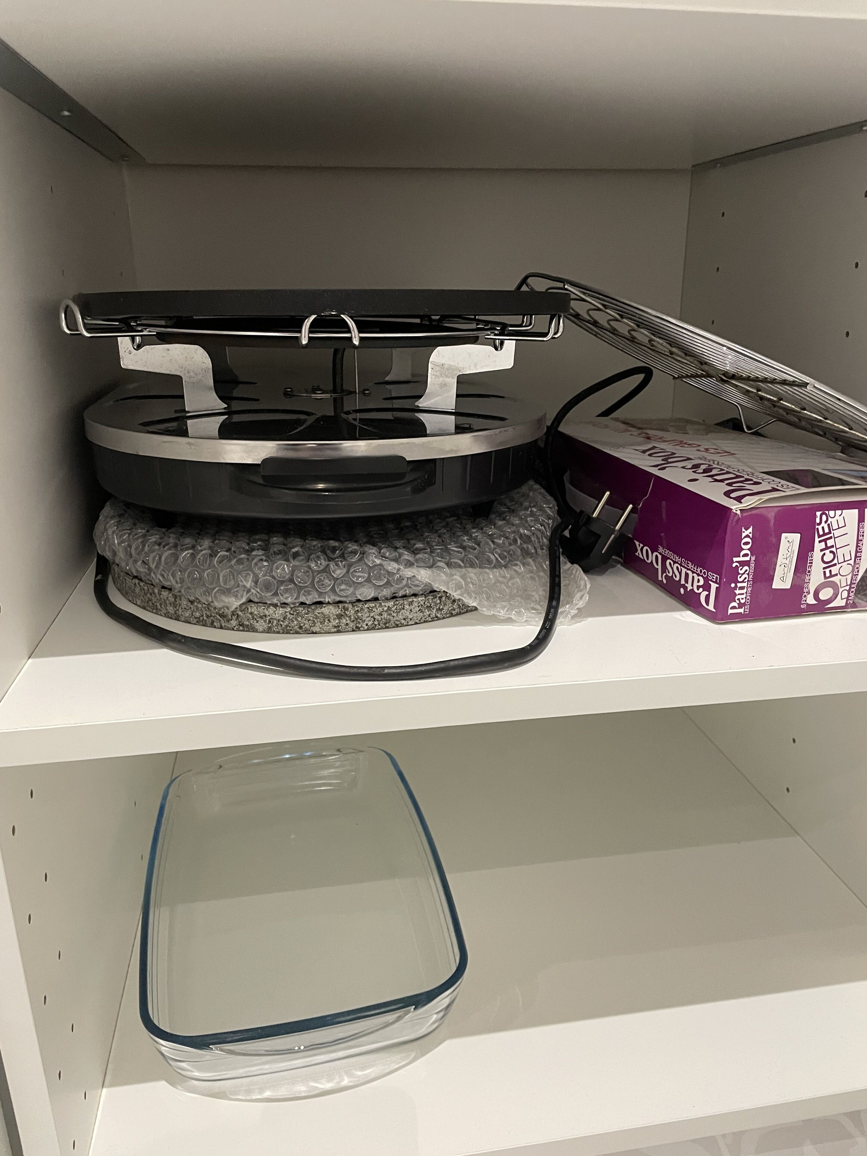 A kitchen with a microwave, a box of paper towels, and a glass baking dish on a shelf.