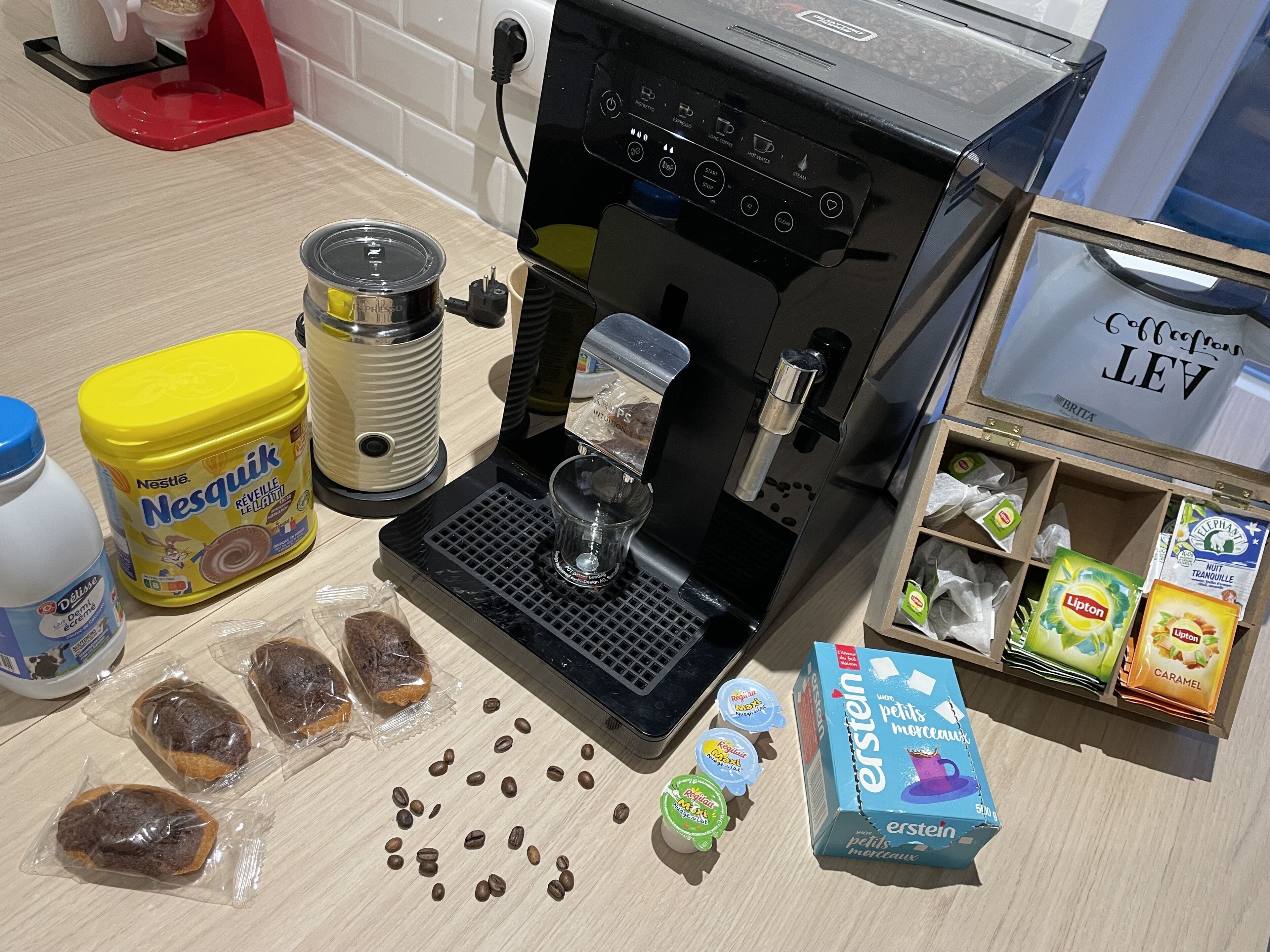 Eine Küche mit Kaffeemaschine, Kaffeemühle, einer Nesquik-Glaskaraffe, einer Packung Lipton-Tee und einer Packung Petit Méréaux.