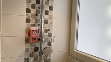 A shower with a rain showerhead and handheld showerhead, a soap dish, and a towel rack.