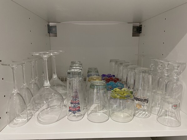 Una mensola con diversi bicchieri, tra cui calici da vino e bicchieri tumbler, alcuni con etichette.